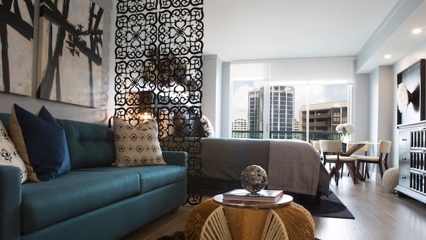 A modern living room with a teal sofa, decorative pillows, a round woven coffee table, and a view of high-rise buildings through large windows. - Deluxe Studio in Coconut Grove-city & Bay Views...includes Parking (Miami)