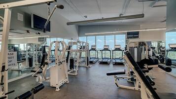 A modern gym with various exercise equipment, large windows, and a city view.