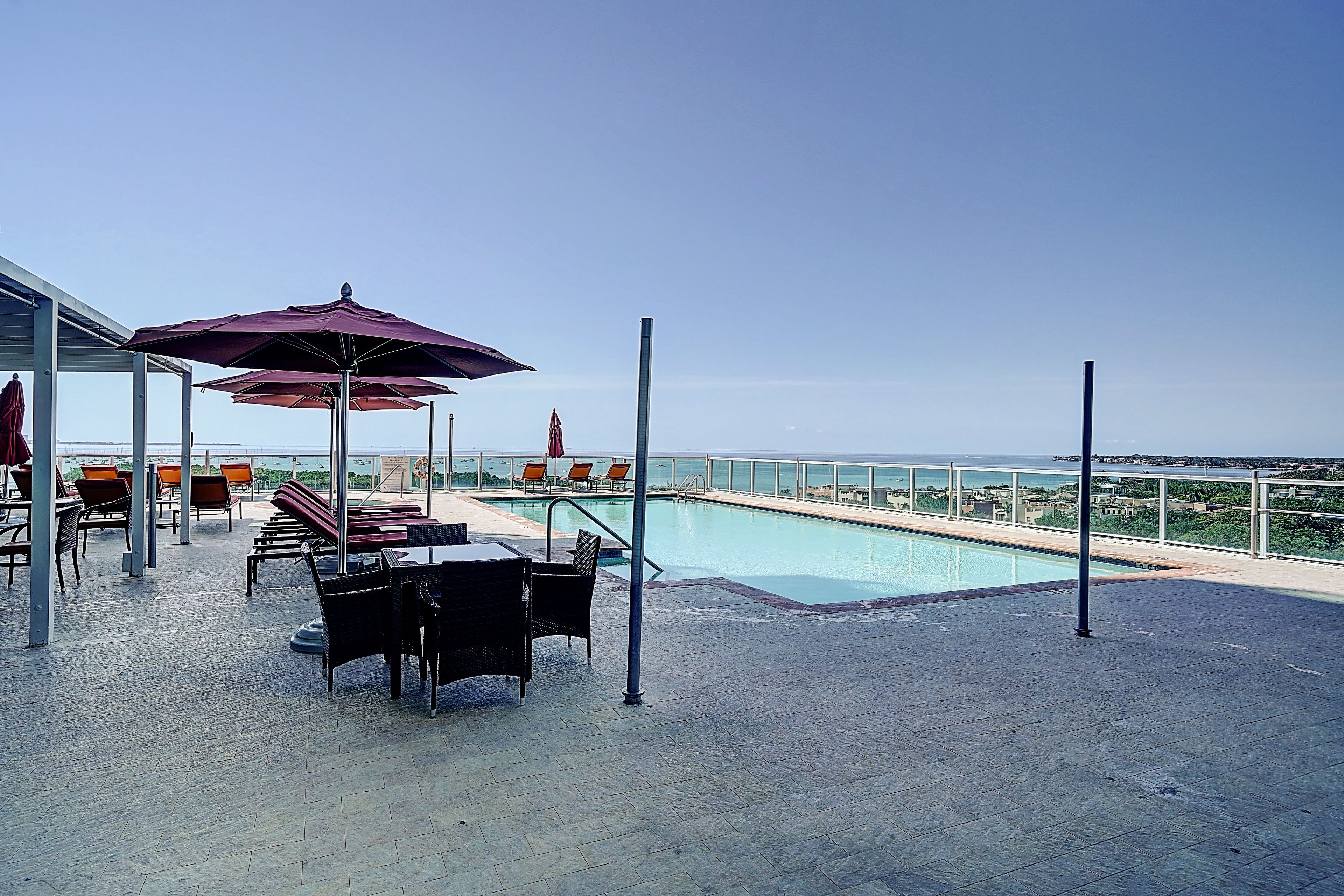 A rooftop pool area with seating and umbrellas, overlooking a cityscape.