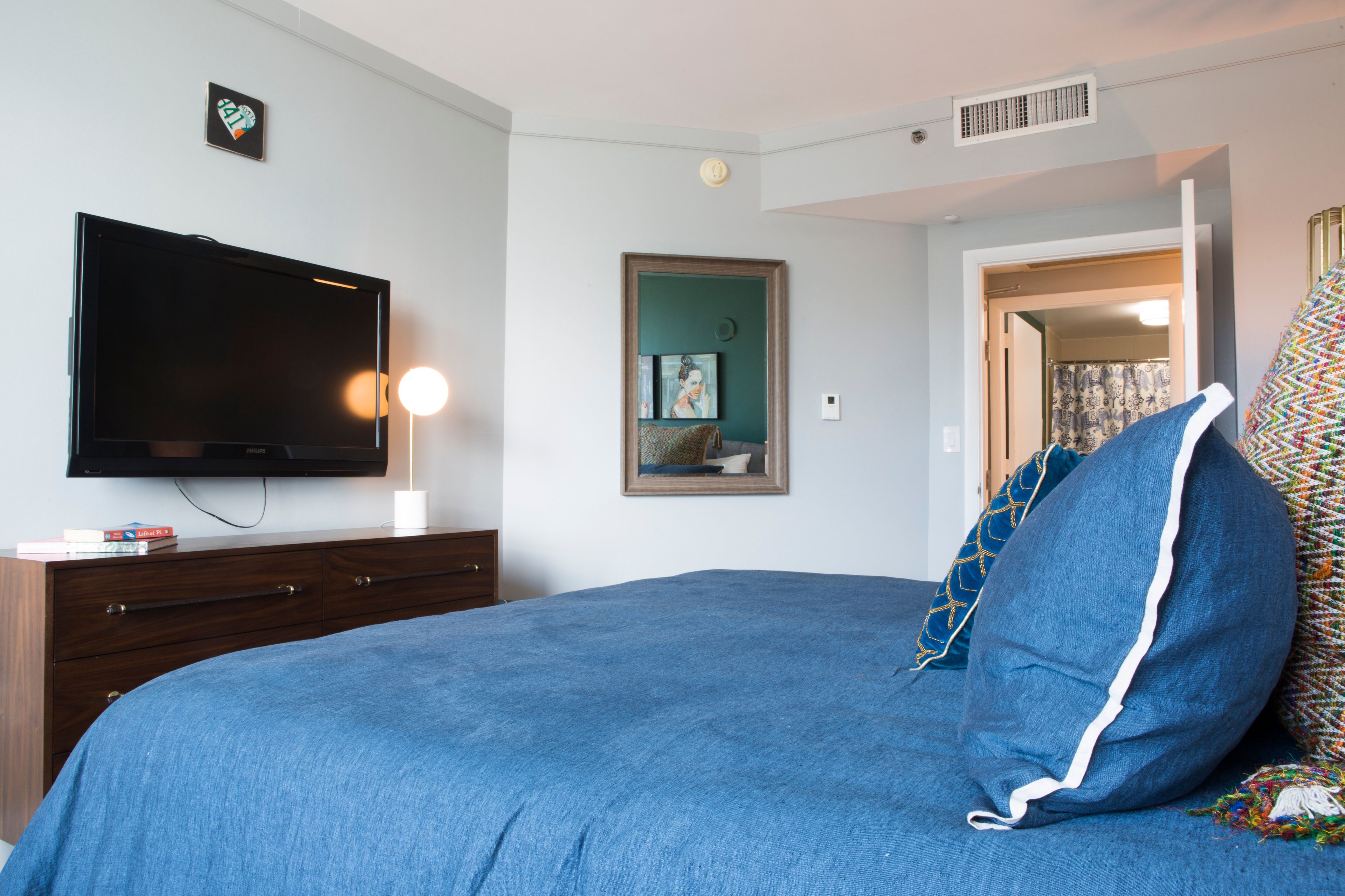 A bedroom with a bed, a television, a dresser, and a door leading to another room.