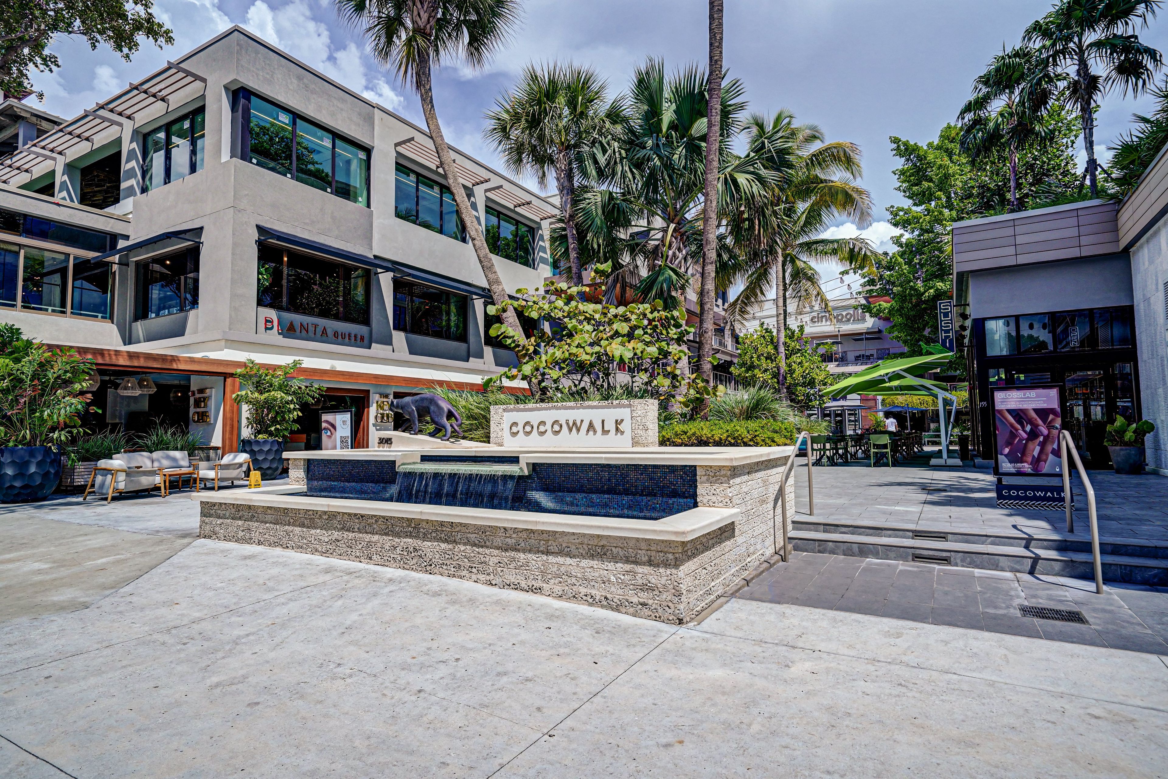 A modern building with a sign reading 'Cocowalk' and a small water feature with a stone wall.