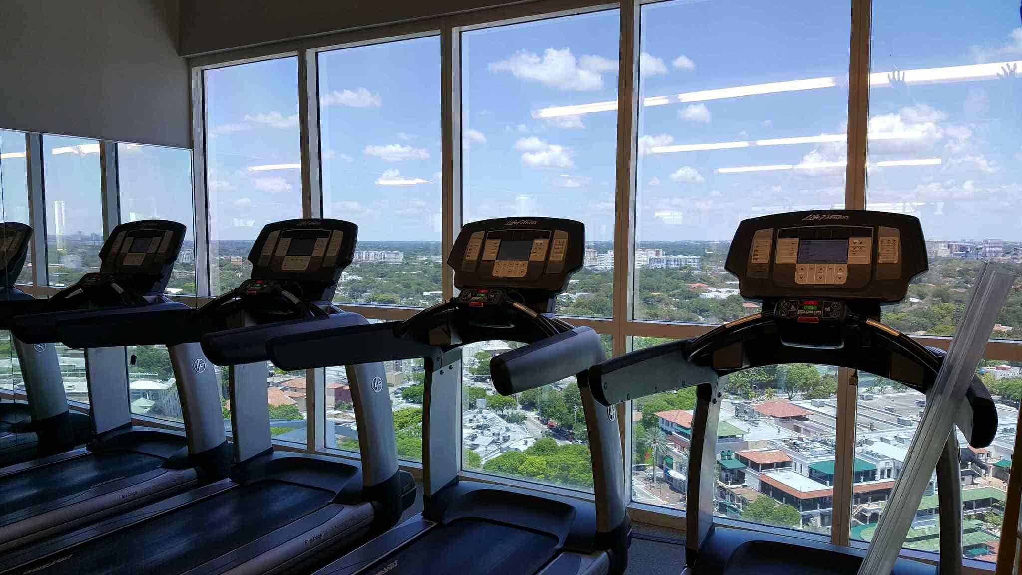 A gym with treadmills and a large window offering a city view.