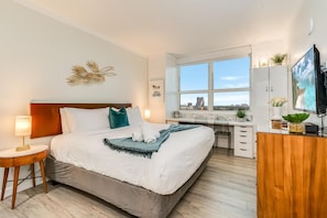 Et hotelværelse med seng, natbord, skrivebord og fjernsyn.
