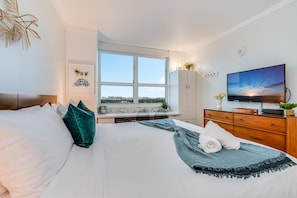 Et hotelværelse med en stor seng, et fjernsyn, et vindue med udsigt over byen og et skrivebord med en plante.