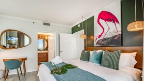 A hotel room with a bed, a desk, a mirror, a bathroom, and a painting of a flamingo. - Elegant 2BR Condo at Hotel Arya Full Kitchen, Wraparound Views, Washer/dryer, 2 Parking Spots (Miami)