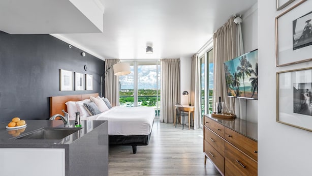 A modern hotel room with a bed, a desk, a TV, and a view of the outdoors. - Modern Grove Studio Parking & Washer/dryer Included (Miami)