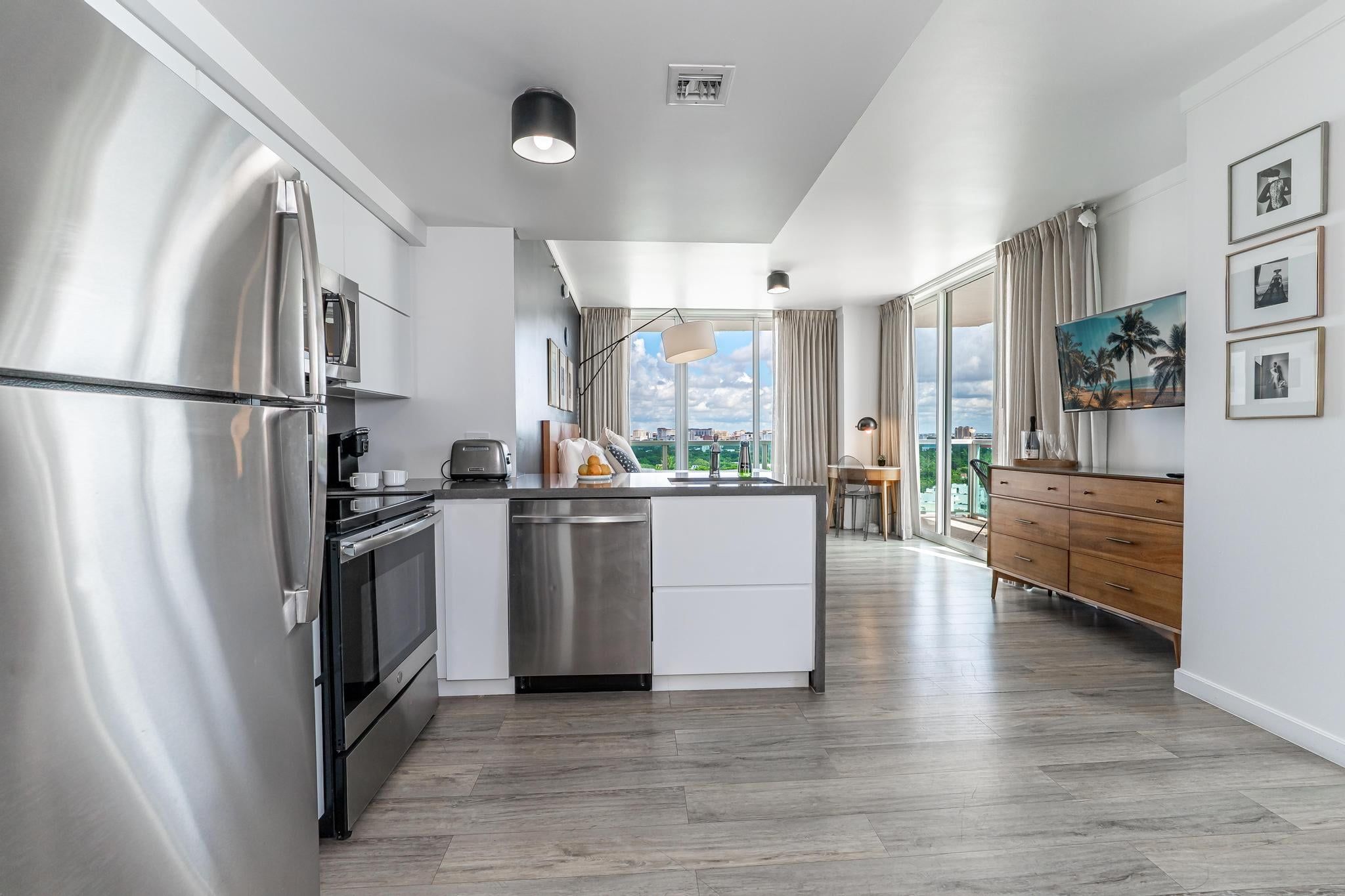 A modern kitchen with stainless steel appliances, a central island, and a view of the city through large windows.