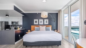 A modern bedroom with a large bed, a bedside table, a nightstand, a ceiling light, a window with a view, and a kitchenette with a microwave and refrigerator. - Modern Grove Studio Parking & Washer/dryer Included (Miami)