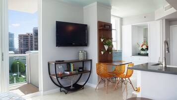 Un apartamento moderno con una televisión de pantalla plana montada en la pared, un comedor con sillas naranjas y una cocina con grifo de acero inoxidable.