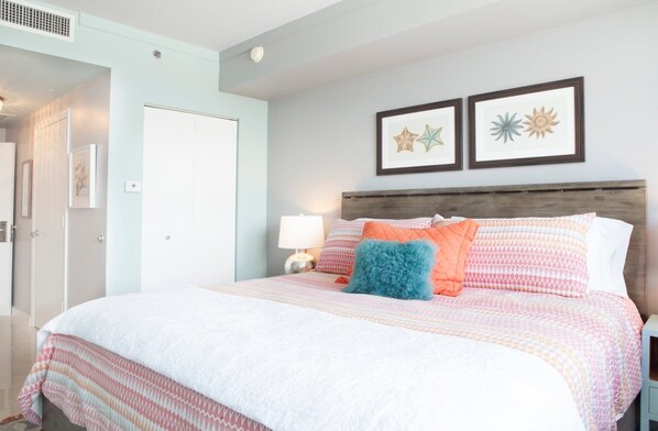 Un dormitorio con cama, mesita de noche, lámpara de pared y dos cuadros enmarcados.