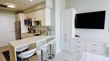 Cocina moderna con una isla central, taburetes de bar, televisor de pantalla plana y cama con colcha blanca.