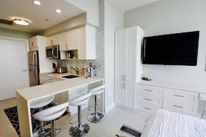 Cocina moderna con una isla central, taburetes de bar, televisor de pantalla plana y cama con colcha blanca.