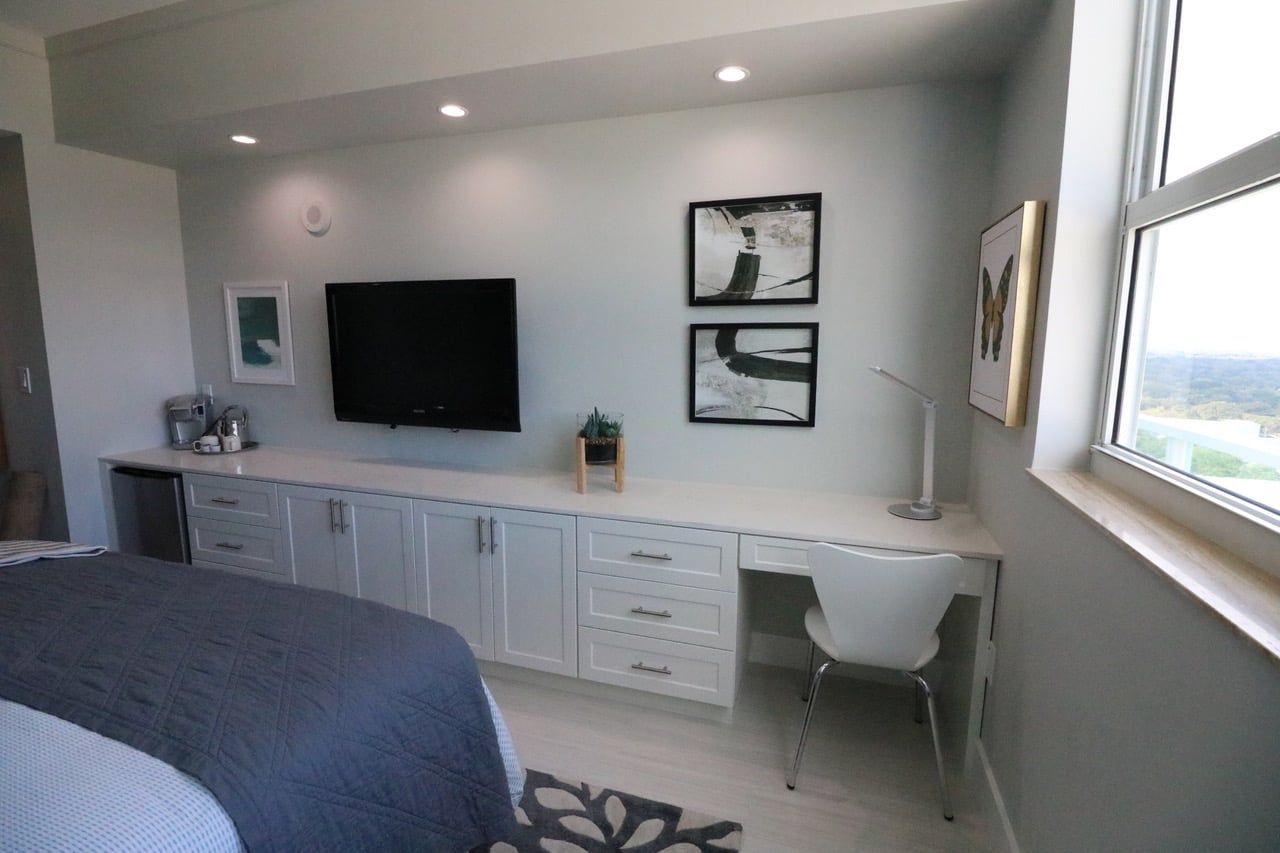 Un dormitorio con cama, escritorio, silla, televisor y cuadros en la pared.