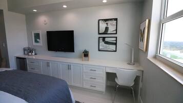 Un dormitorio con cama, escritorio, silla, televisor y cuadros en la pared.