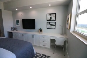 Un dormitorio con cama, escritorio, silla, televisor y cuadros en la pared.