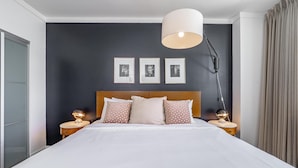 Ett modernt hotellrum med en stor säng, två sängbord med lampor, en mörk vägg och tre inramade tavlor.