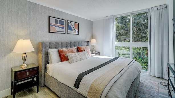 Een slaapkamer met een groot bed, twee nachtkastjes, een raam met gordijnen, en twee ingelijste foto's aan de muur.