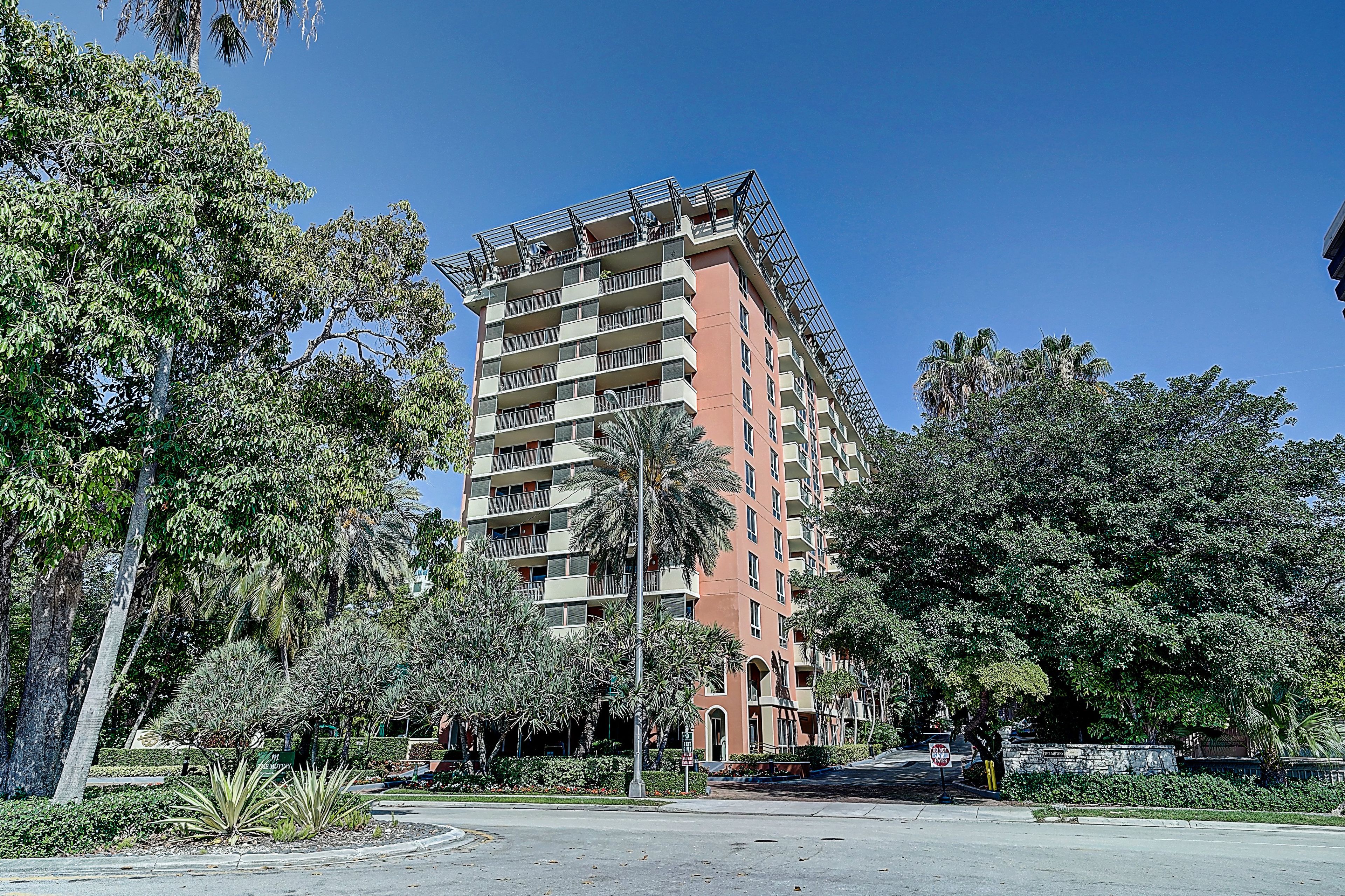 A multi-story hotel with balconies, surrounded by lush greenery and palm trees.