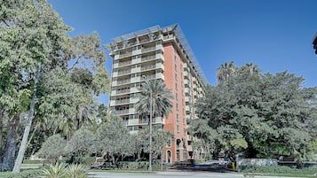A multi-story hotel with balconies, surrounded by lush greenery and palm trees.