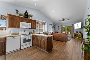 A modern kitchen with wooden cabinets, a microwave, stove, and a dining area with a brown sofa. - Cozy at the Cove - Pool Access (Branson)