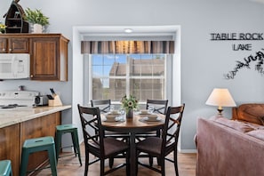 A modern kitchen with a dining area, wooden cabinets, a microwave, and a window with blinds. - Cozy at the Cove - Pool Access (Branson)