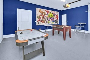 Een kamer met een tafelvoetbaltafel, een pingpongtafel en een grote muurschildering met superhelden.