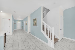 A hallway with a marble floor, light blue walls, white doors, and a staircase with white railings. - Disney Area Villa with Private Pool Spa & Theater (Four Corners)