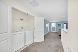 A laundry room with two washing machines and a dryer, a door leading to another room, and a carpeted floor. - Disney Area Villa with Private Pool Spa & Theater (Four Corners)
