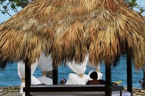 A thatched-roof structure with a bench and a person sitting underneath. - 1BR VIP Residence Suites, Gold band, All-Inclusive, Puerto Plata, DR (Puerto Plata)