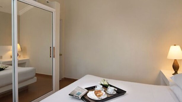 A hotel room with a bed, a bedside table with a lamp, a tray with breakfast items, and a sliding door leading to another room. - 1BR VIP Residence Suites, All-Inclusive, Gold band, Puerto Plata, DR (Puerto Plata)