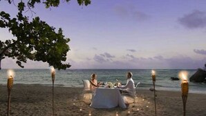 A beachside dining setup with a table and chairs under a tree, surrounded by candles. - 1BR VIP Residence Suites, All-Inclusive, Gold band, Puerto Plata, DR (Puerto Plata)