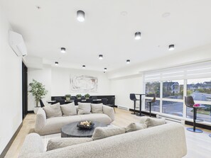 Una sala de estar moderna con sofá, una mesita de centro y un ventanal que ofrece vistas del barrio.