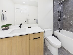 Ein modernes Badezimmer mit einem weißen Waschbecken, Holzschränken, einer Toilette und einer Duschkabine mit Marmorwand.