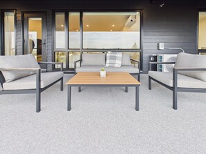 A modern outdoor seating area with a sofa and two chairs, a wooden table, and a potted plant. - Scenic 3BR Mountain and Lake Haven in Bear Mountain (Langford)
