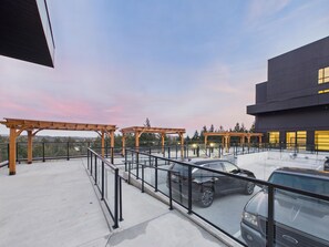 Un estacionamiento en la azotea con un coche, pérgolas de madera y un edificio moderno con grandes ventanales.