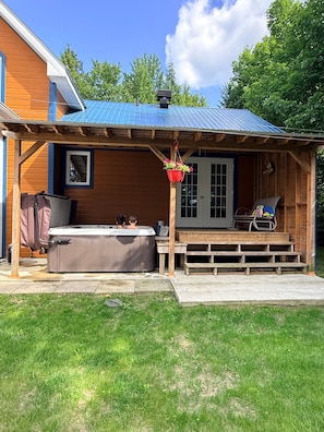 En træhytte med en overdækket terrasse, et spabad og en blomsterkasse.