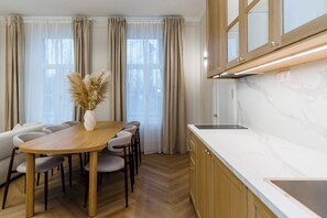 A modern kitchen with wooden cabinets, a marble countertop, and a dining area with a wooden table and chairs. - Elegant Apartment | Fireplace | 20 min Old Town (Riga)