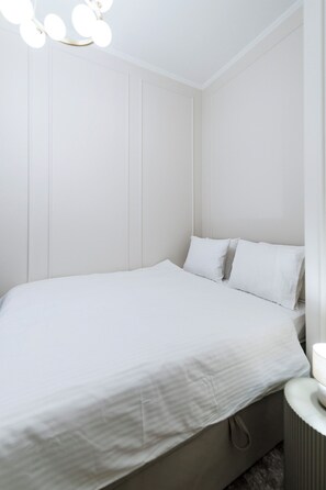 A minimalist bedroom with a bed, bedside table, and a wall-mounted light fixture. - Elegant Apartment | Fireplace | 20 min Old Town (Riga)