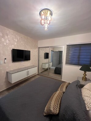 Une chambre à coucher comprenant un lit, une télévision, une armoire, un miroir et un luminaire fixé au plafond.
