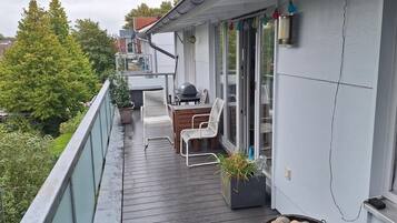 Ein überdachter Außenbereich mit Holzdeck, Grill und Sitzgelegenheit.
