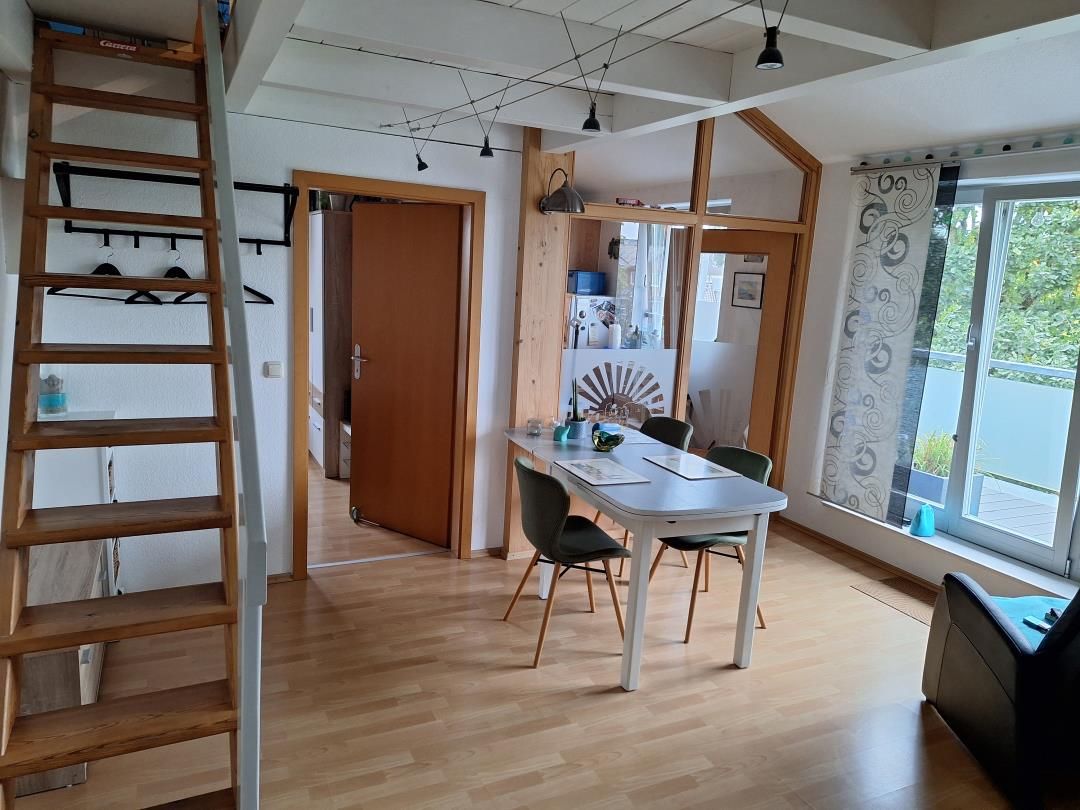 Ein Zimmer mit Holzboden, einem Esstisch mit Stühlen, einer Leiter und einem Fenster mit Vorhängen.