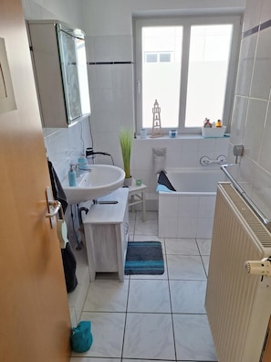 Ein Badezimmer mit Waschbecken, Spiegel, Fenster, Badewanne und Heizkörper.
