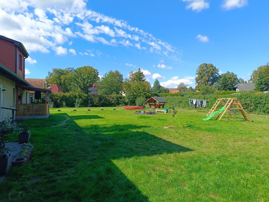 Ein Garten mit Rasenfläche, einer Holzspielanlage und einem roten Boot.