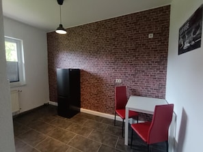 A room with a brick wall, a white table with red chairs, a black cabinet, and a hanging light fixture. - Vrbo Property (Joachimsthal)