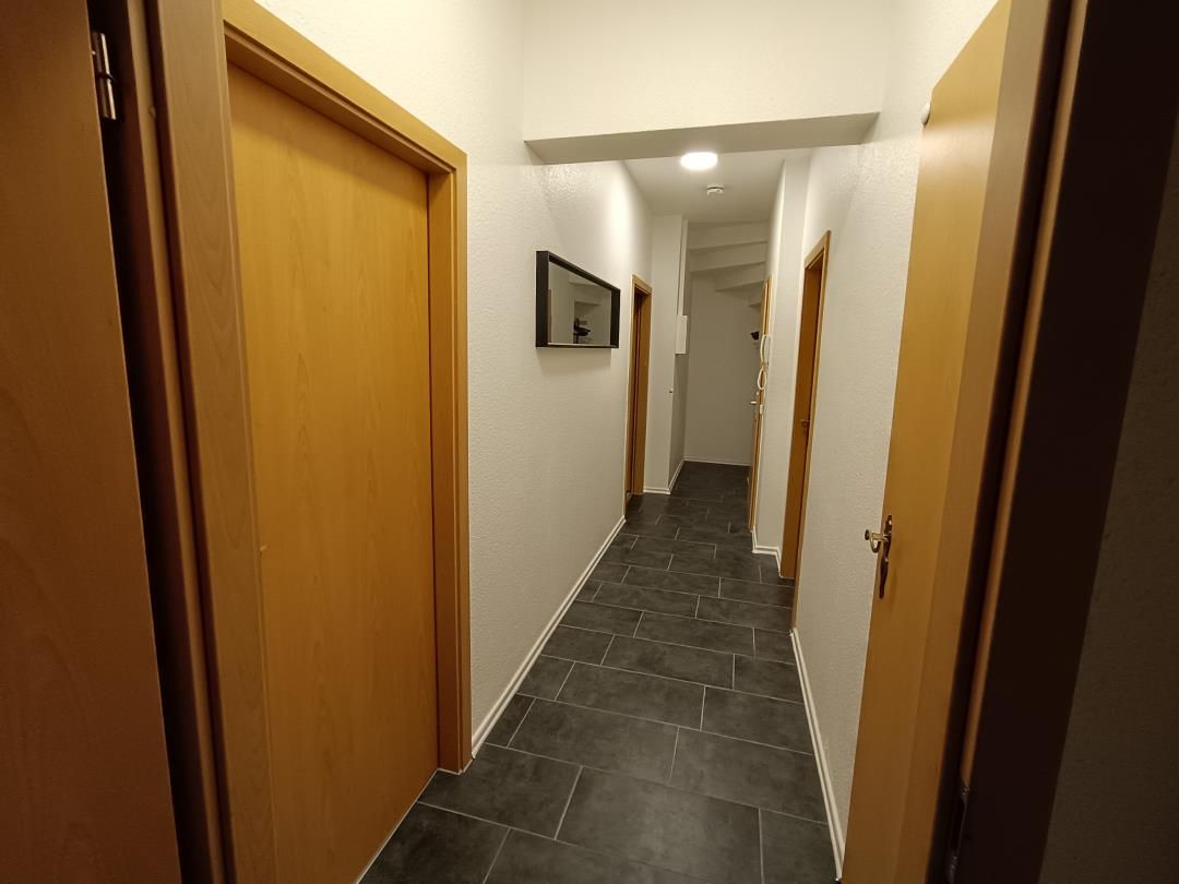 Ein Korridor mit Holztüren, einem Fliesenboden und einem Spiegel an der Wand.