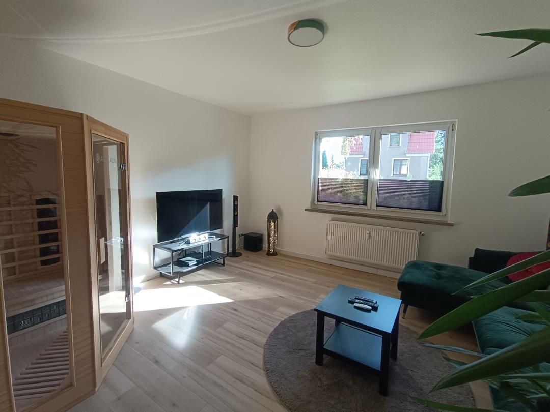 Ein Wohnzimmer mit Fernseher, einer Couch, einem Couchtisch und einem Fenster mit Blick auf Gebäude.