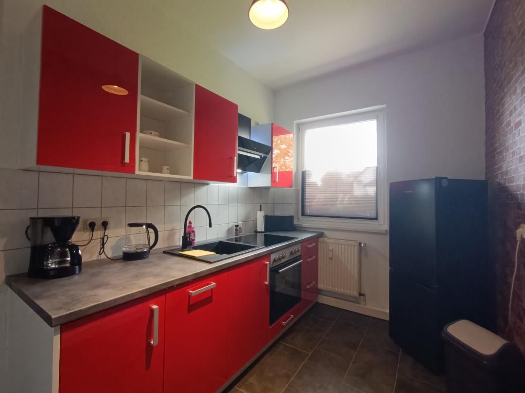 Eine Küche mit roten Schränken, einem schwarzen Kühlschrank und einem Fenster mit Jalousien.