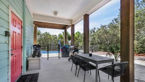 Un patio techado con mesa y sillas, una parrilla y una piscina al fondo.