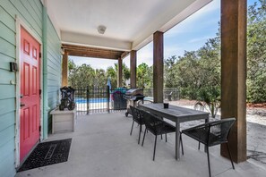 Un patio couvert avec une table et des chaises, un barbecue et une piscine en arrière-plan.