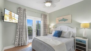 Un dormitorio con cama, mesitas de noche, ventilador de techo, vistas por la ventana y una obra de arte colgada.
